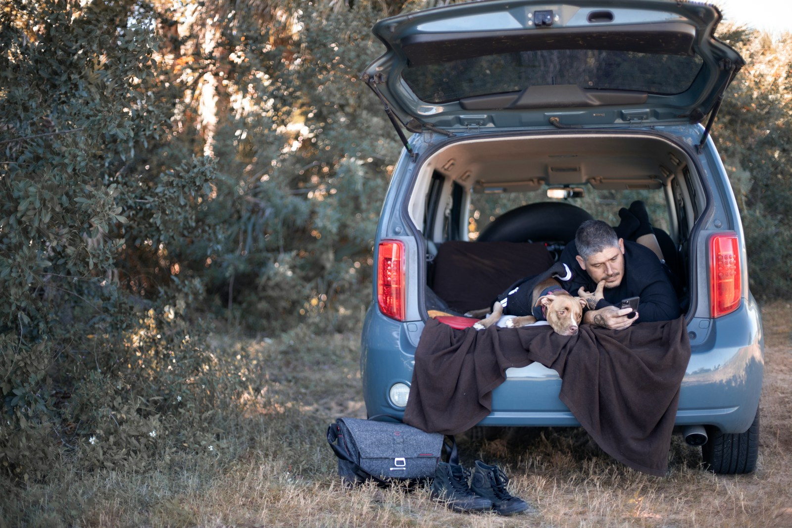 Man sitting in the open back of a blue van at camp, showing the cargo space the best car for hiking and camping needs