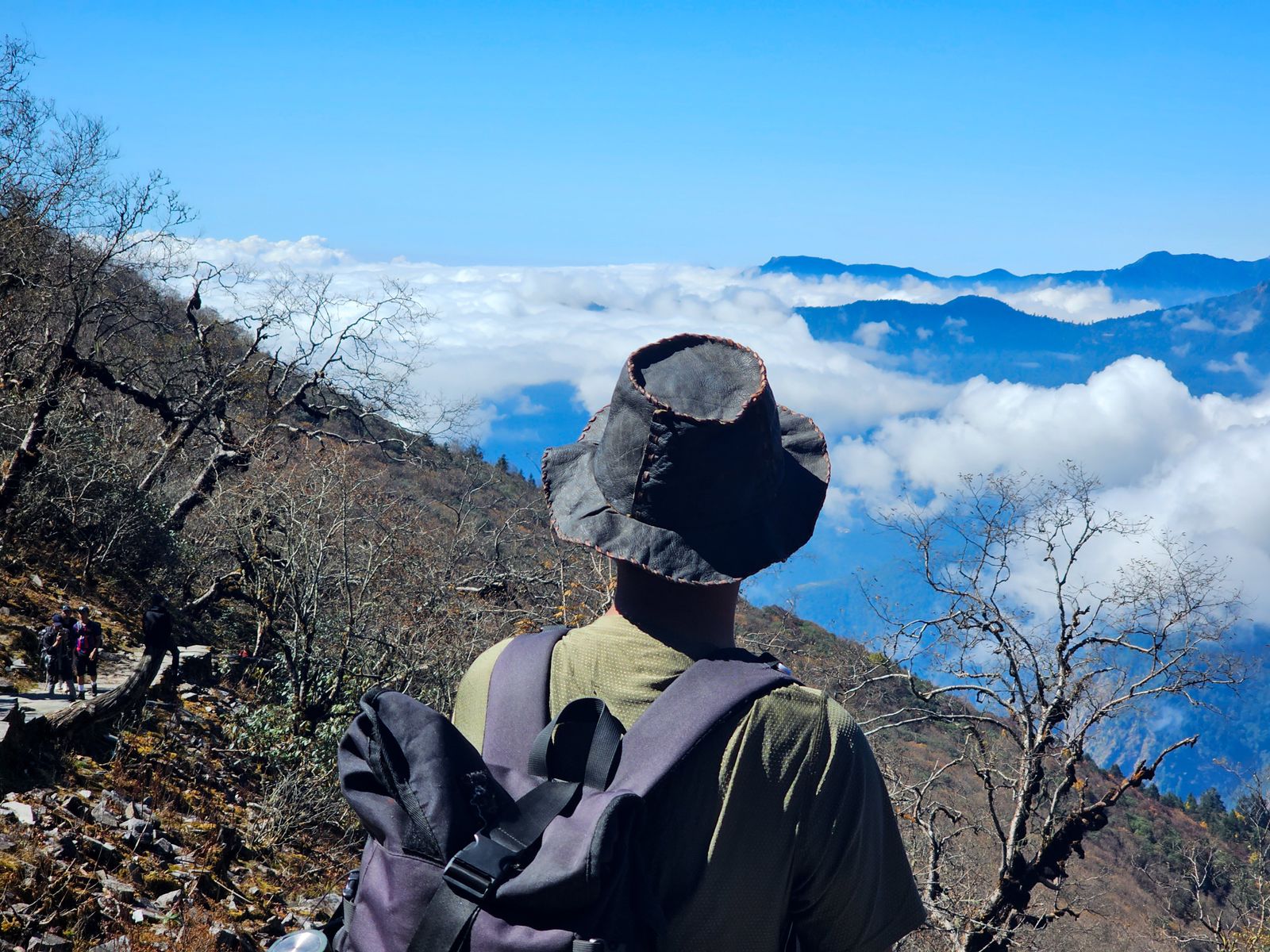Hiker with a backpack and hat overlooking mountains, a reminder to check how a hat for hiking sits with your pack