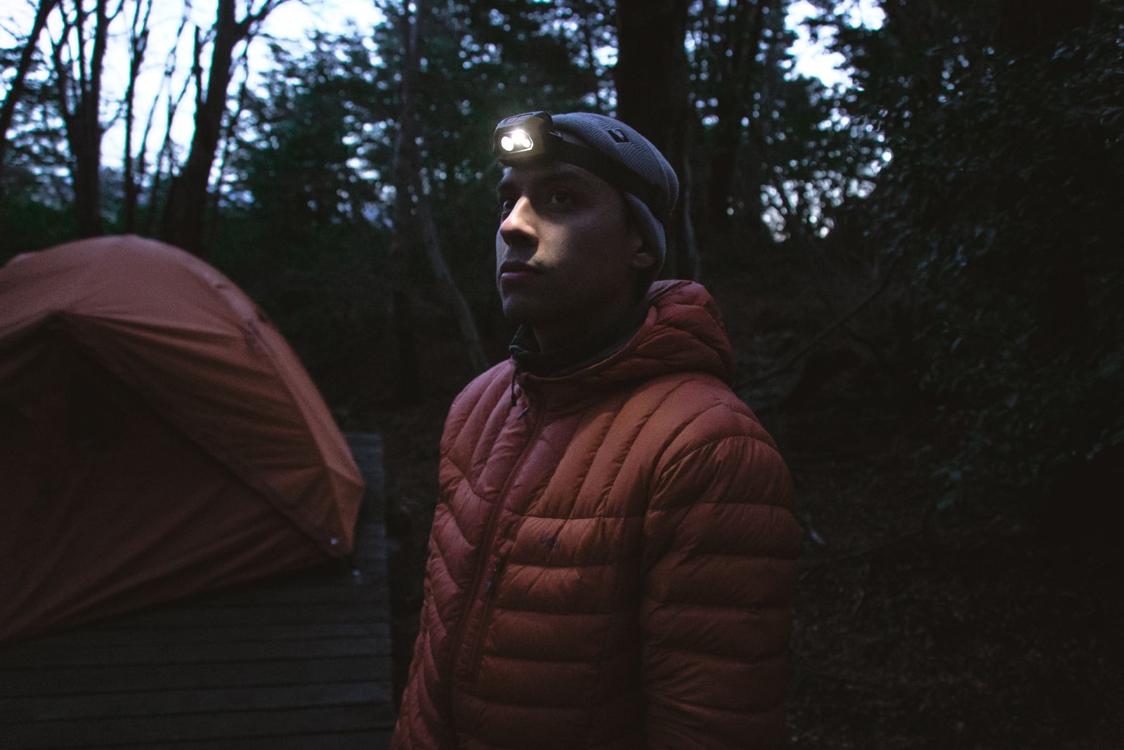 Backpacker wearing a hiking headlamp beside a tent in the forest at night