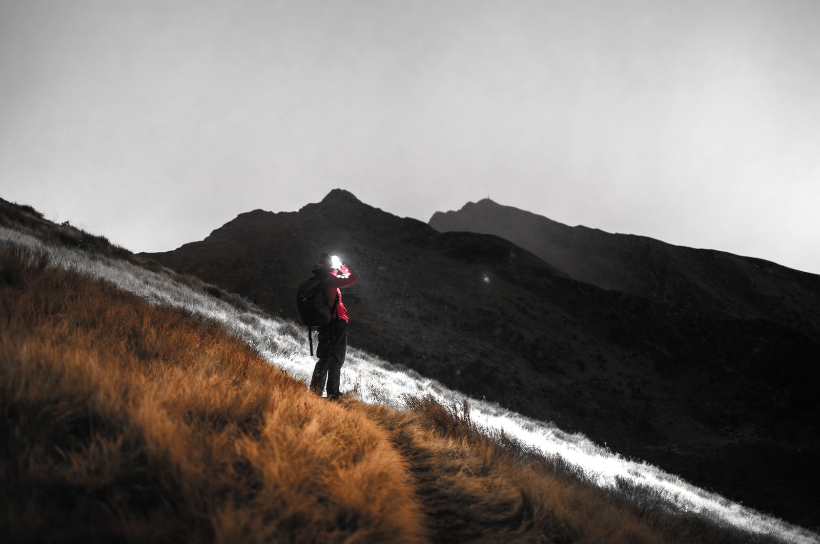 Hiker with a headlamp on a wet mountain path during an overnight hike