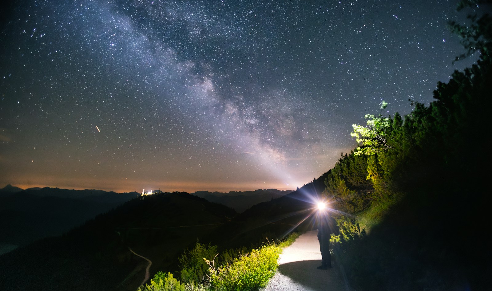 Red light from a headlamp for hiking on a mountain path under the Milky Way