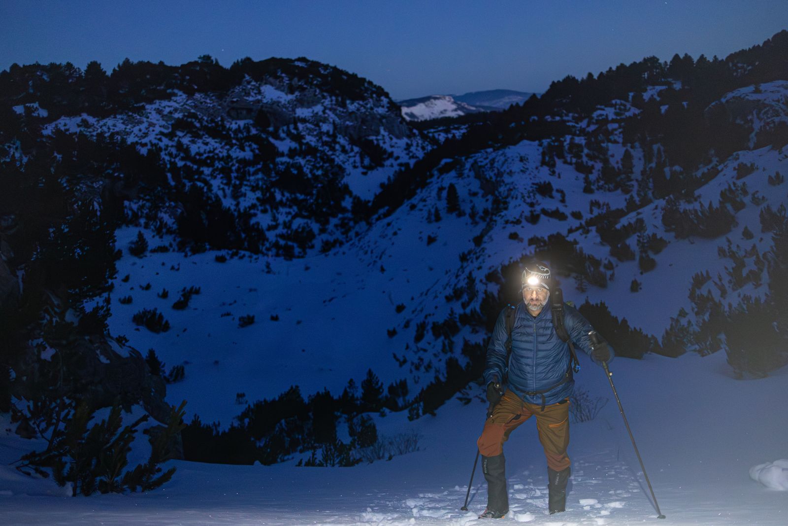 Bright hiking headlamp beam guiding a hiker up a snowy mountain at night