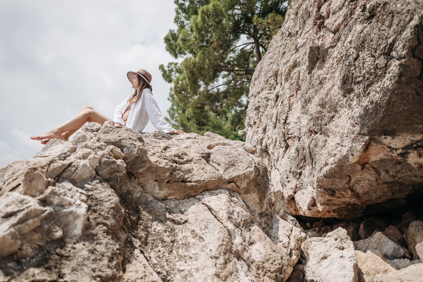 Woman in a white long-sleeve top and hat resting on a rock, showing why light colors suit a hiking hoodie women's fit in summer