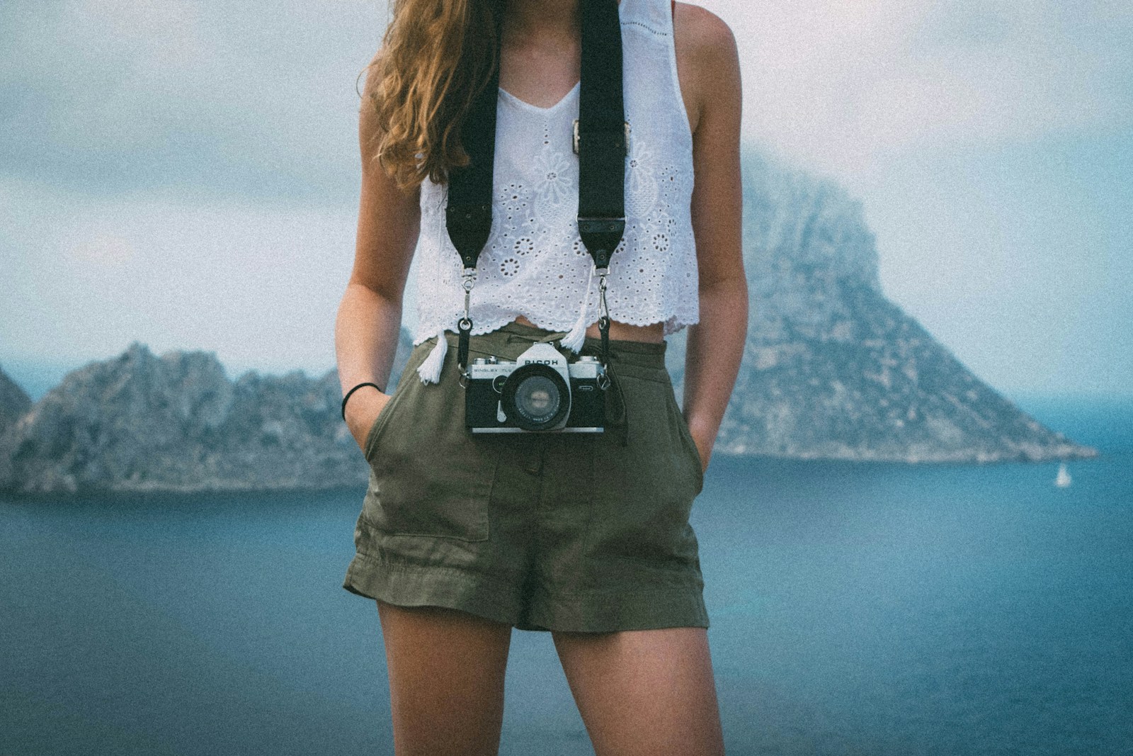 Woman in green shorts holding a camera by the water, a simple hiking shorts women outfit for warm days