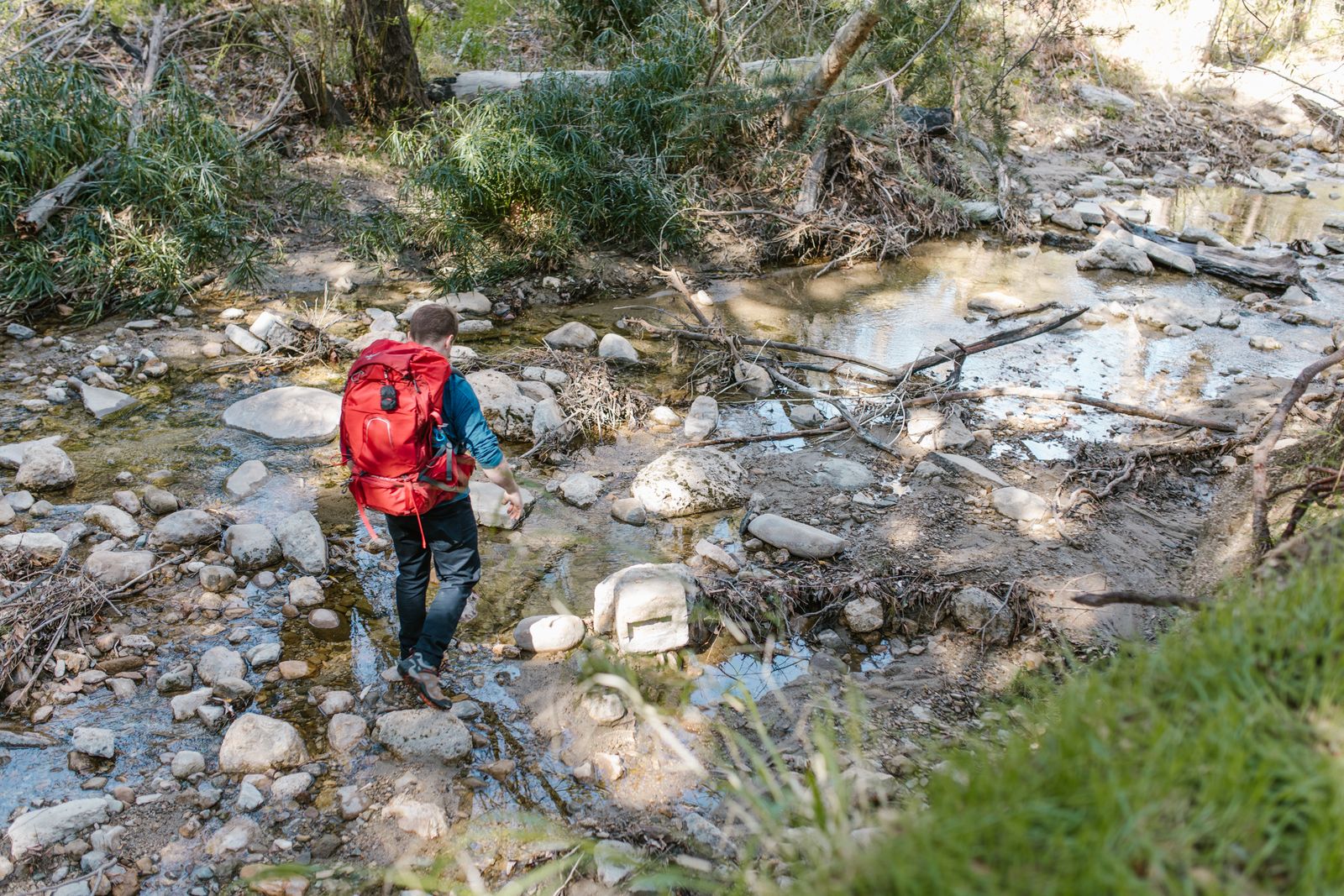 Hiker crossing a rocky forest stream, where a sturdy hiking staff earns its place