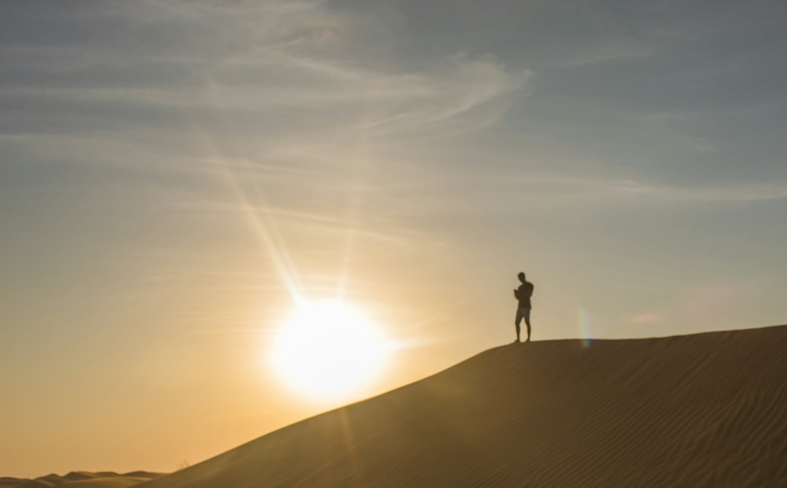 Person standing on top of a sand dune in hot sun, the conditions that decide which hiking hoodie fabric works best in summer