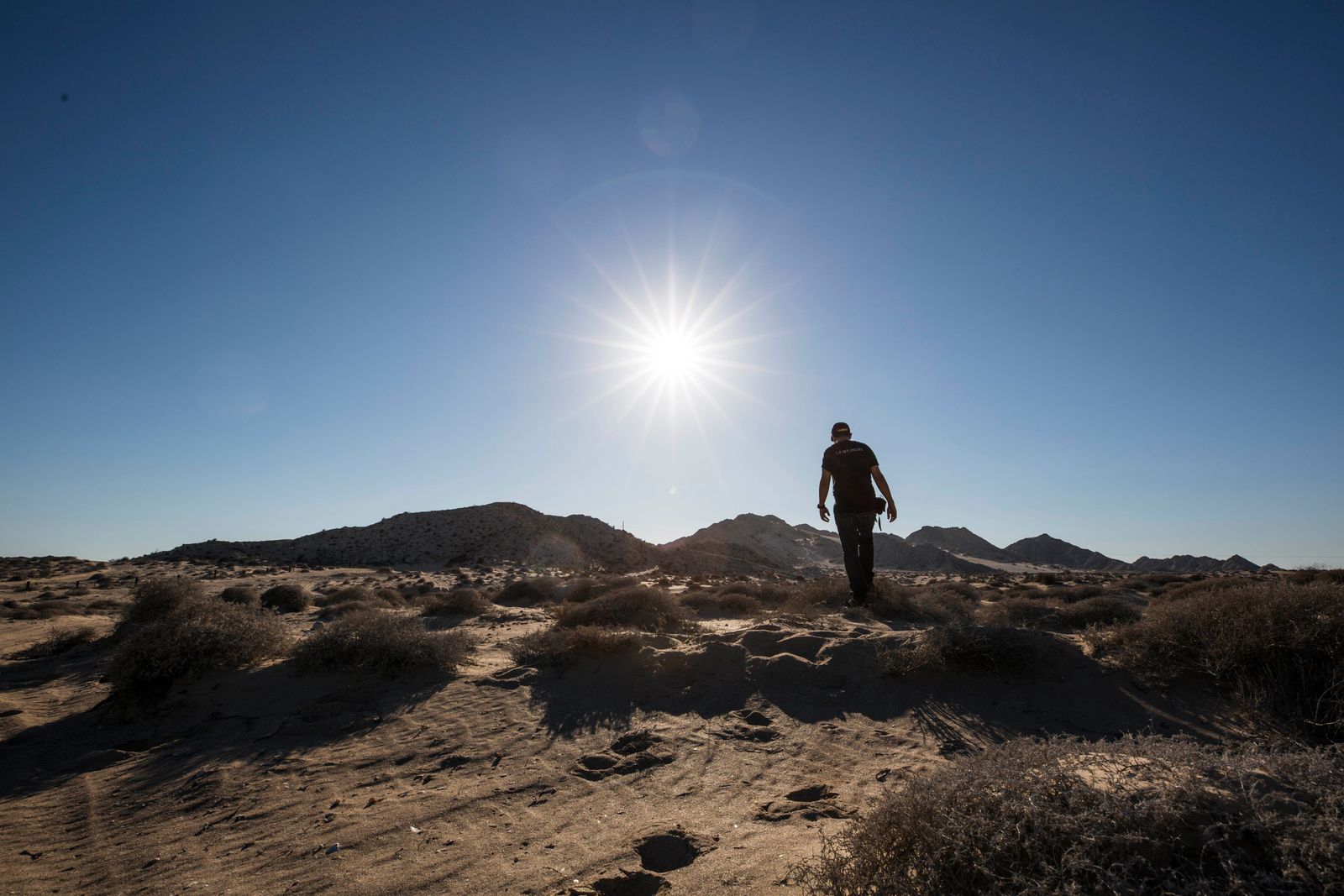Hiker crossing open desert under strong midday sun, where a sun hoodie for hiking pays off