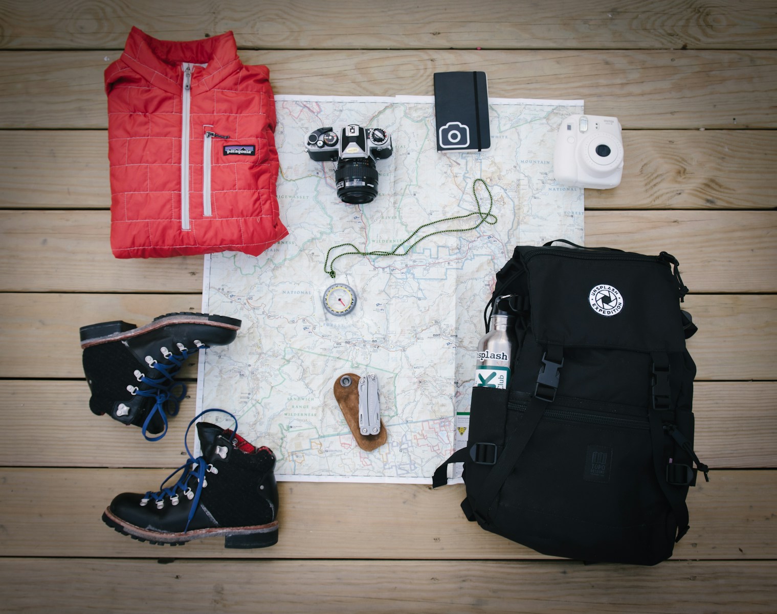 Hiking backpack, boots, jacket and watch laid out on a map, packing the ten essentials for a hike