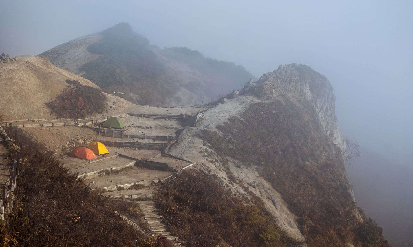 Tents pitched below misty mountains at a damp campsite, where good tent care pays off