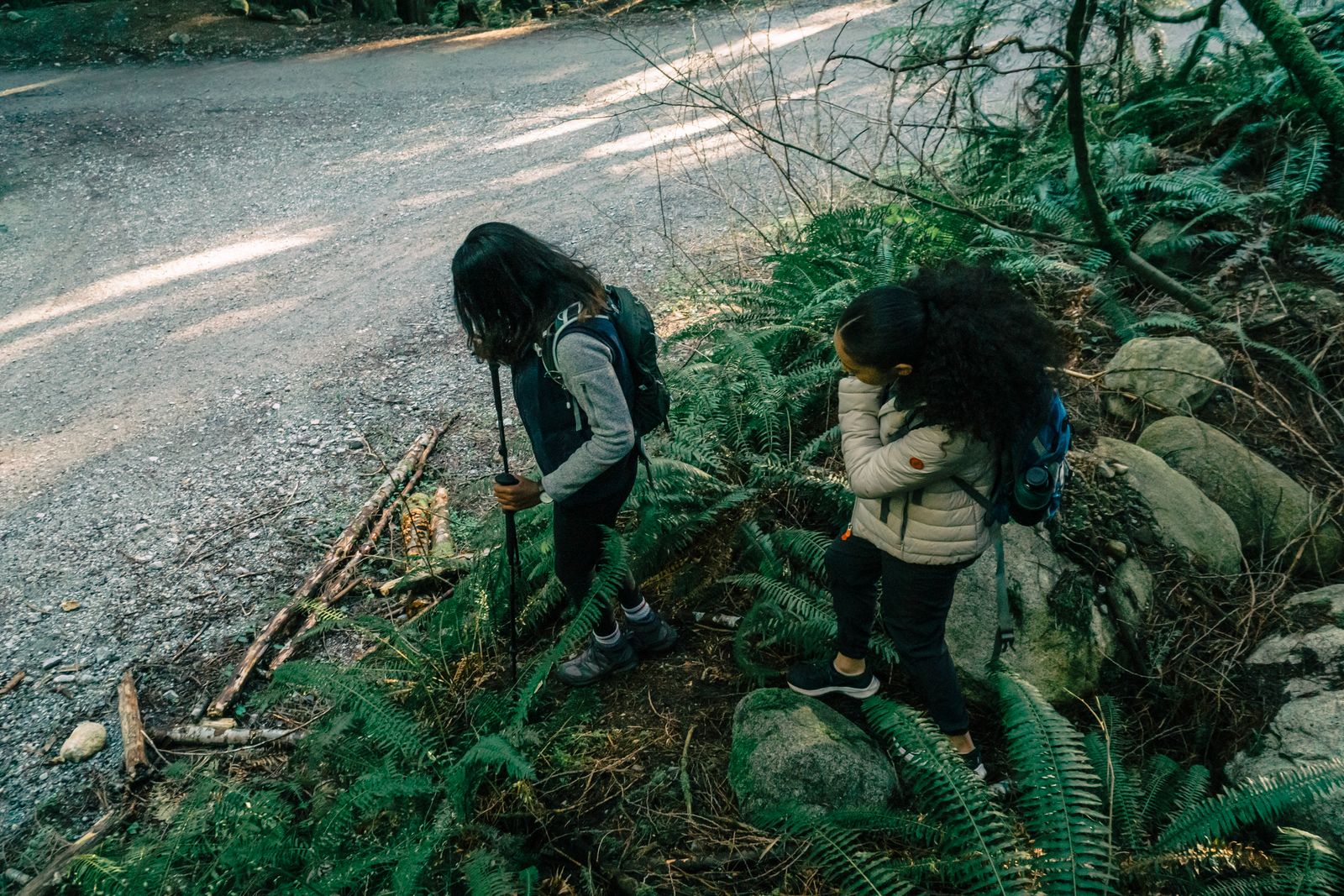 Two women hiking a forest trail through lush vegetation, the everyday terrain trekking shorts womens hikers need to handle